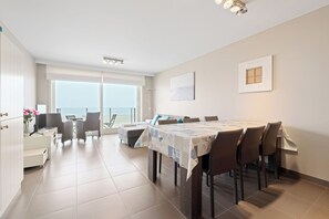 Un vaste espace de salle à manger avec une grande table et des chaises, un balcon offrant une vue agréable et une cuisine moderne.