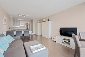 Ein modernes Wohnzimmer mit grauem Sofa, einem Flachbildfernseher und einem Essbereich mit Tisch und Stühlen.
