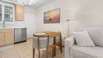 A modern kitchen with a dining area, a sofa, and a painting on the wall.