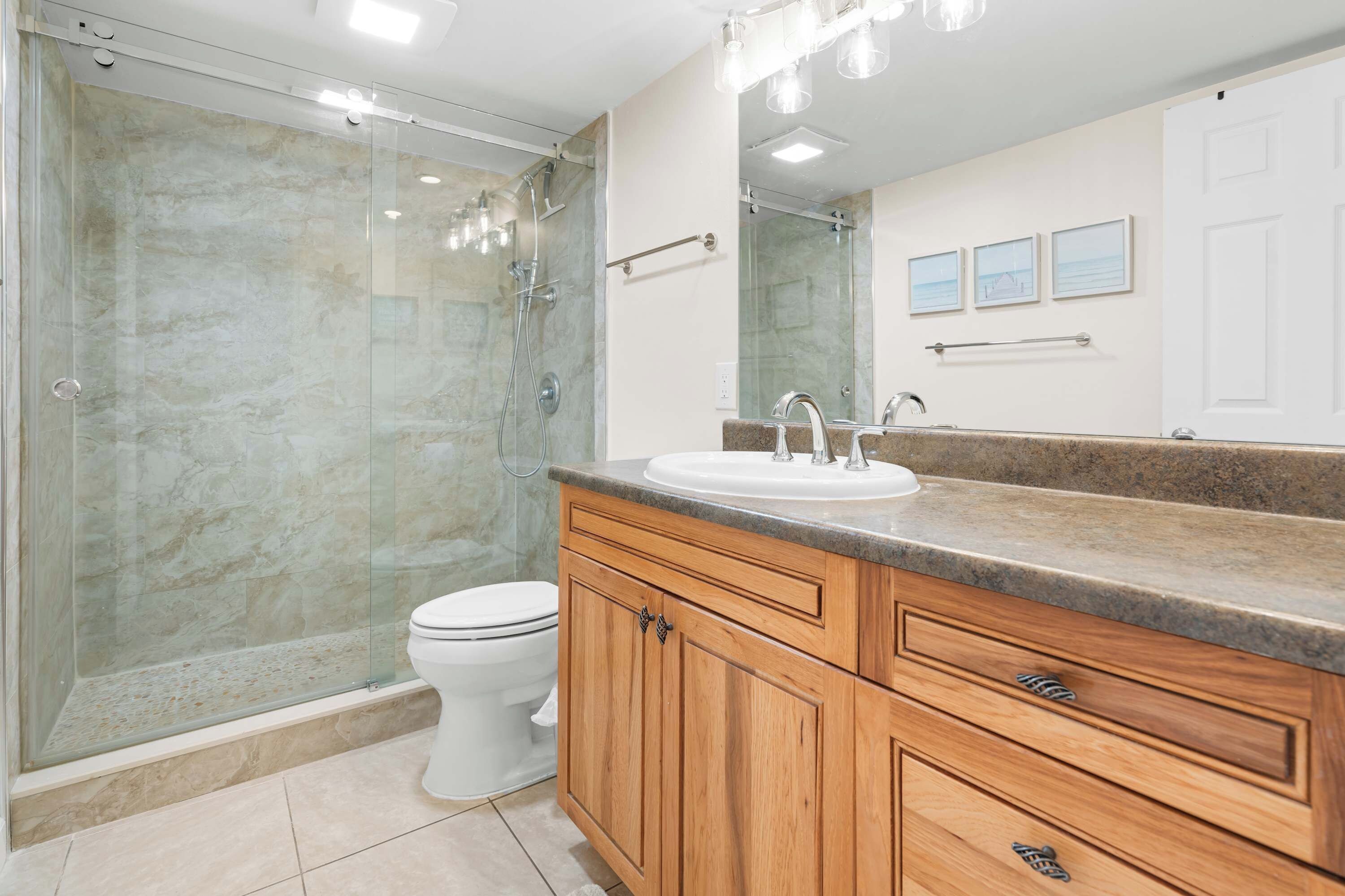 Un baño con ducha envuelta en vidrio, inodoro blanco, armarios de madera y un espejo grande.