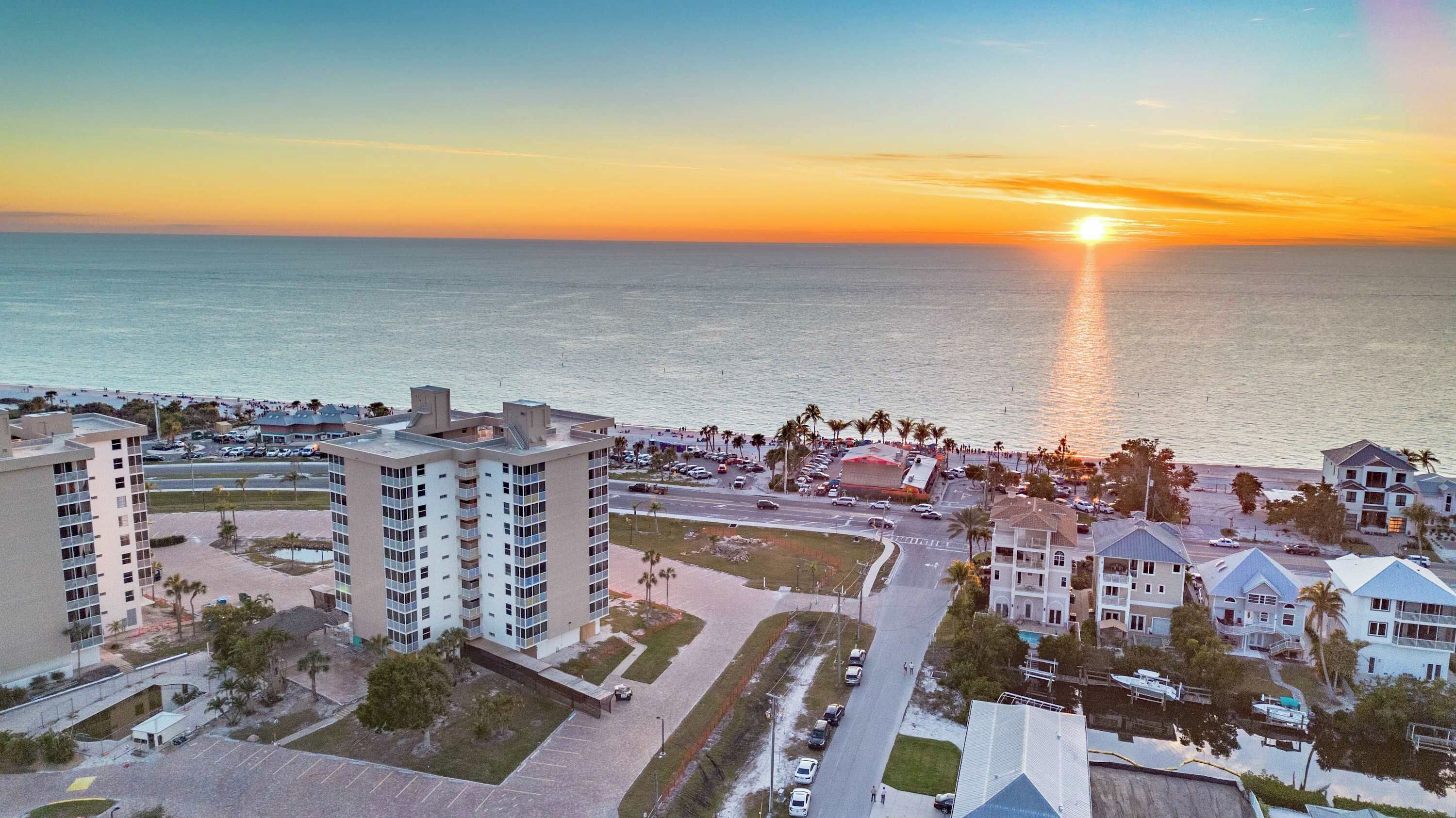 A coastal urban area with high-rise buildings, a marina, and a sunset over the ocean.