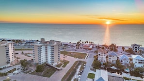 Una zona urbana costera con edificios altos, un puerto deportivo y una puesta de sol sobre el océano.