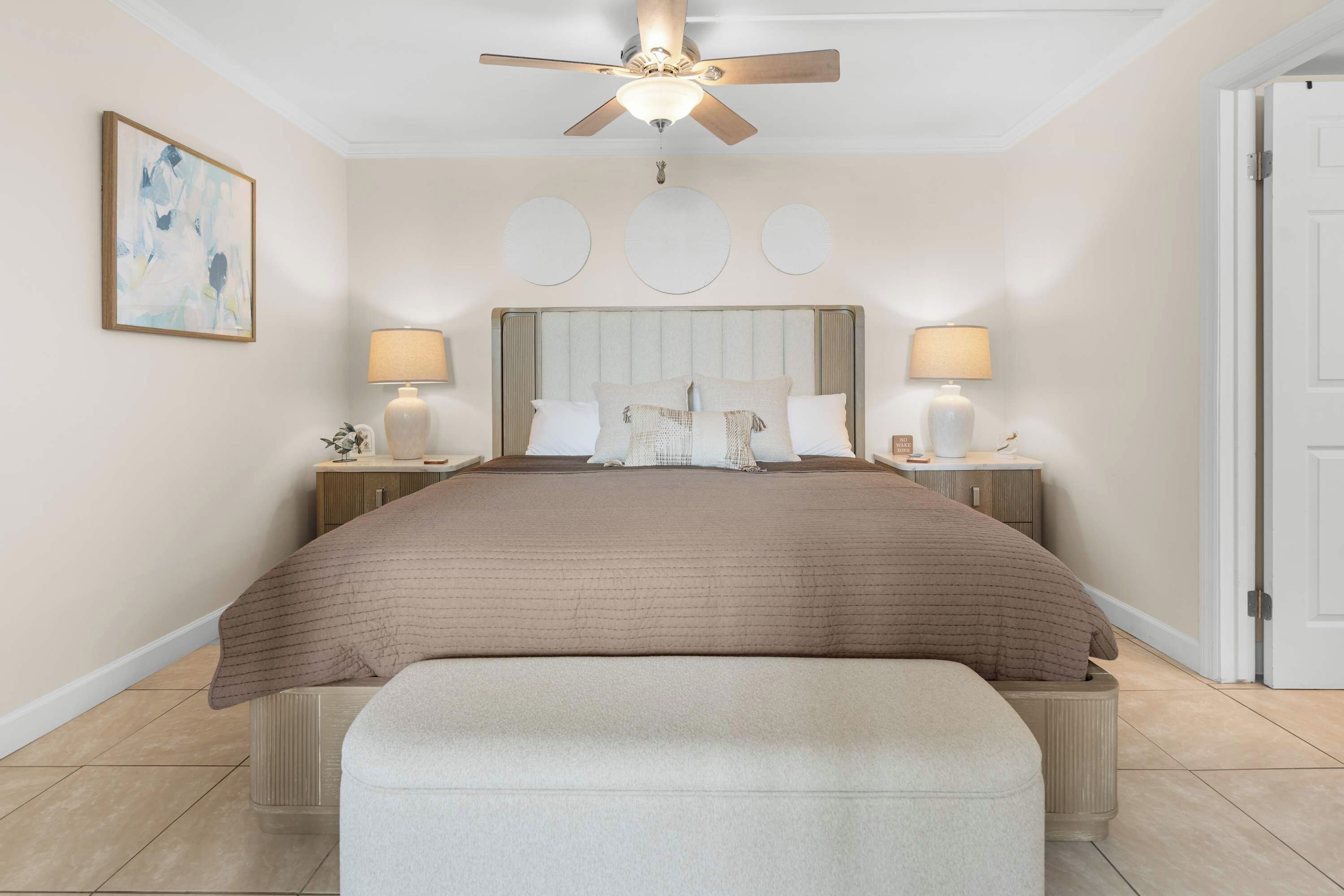 A bedroom with a bed, a bedside table, a nightstand, a ceiling fan, and a door.