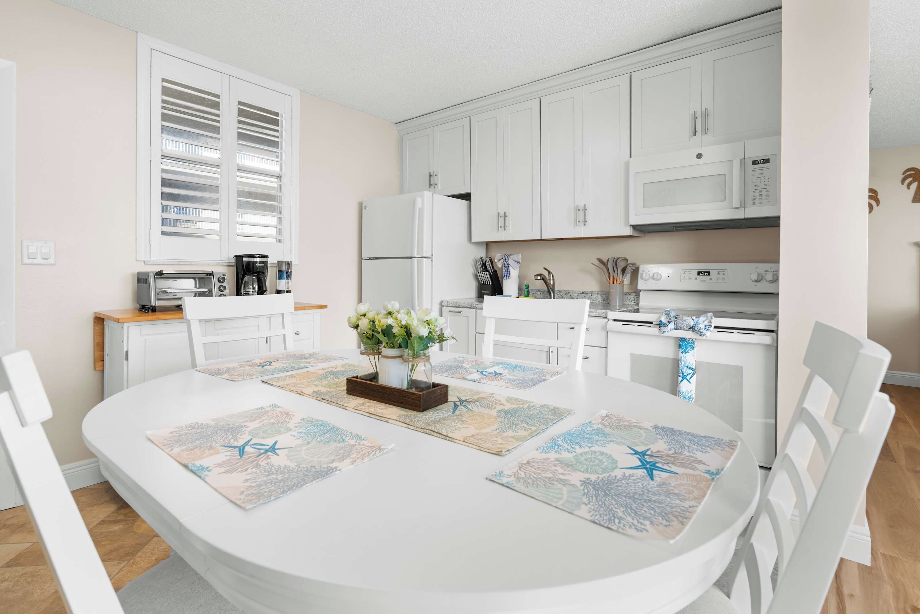 A modern kitchen with white cabinetry, a built-in microwave, and a dining area with a round table and chairs.