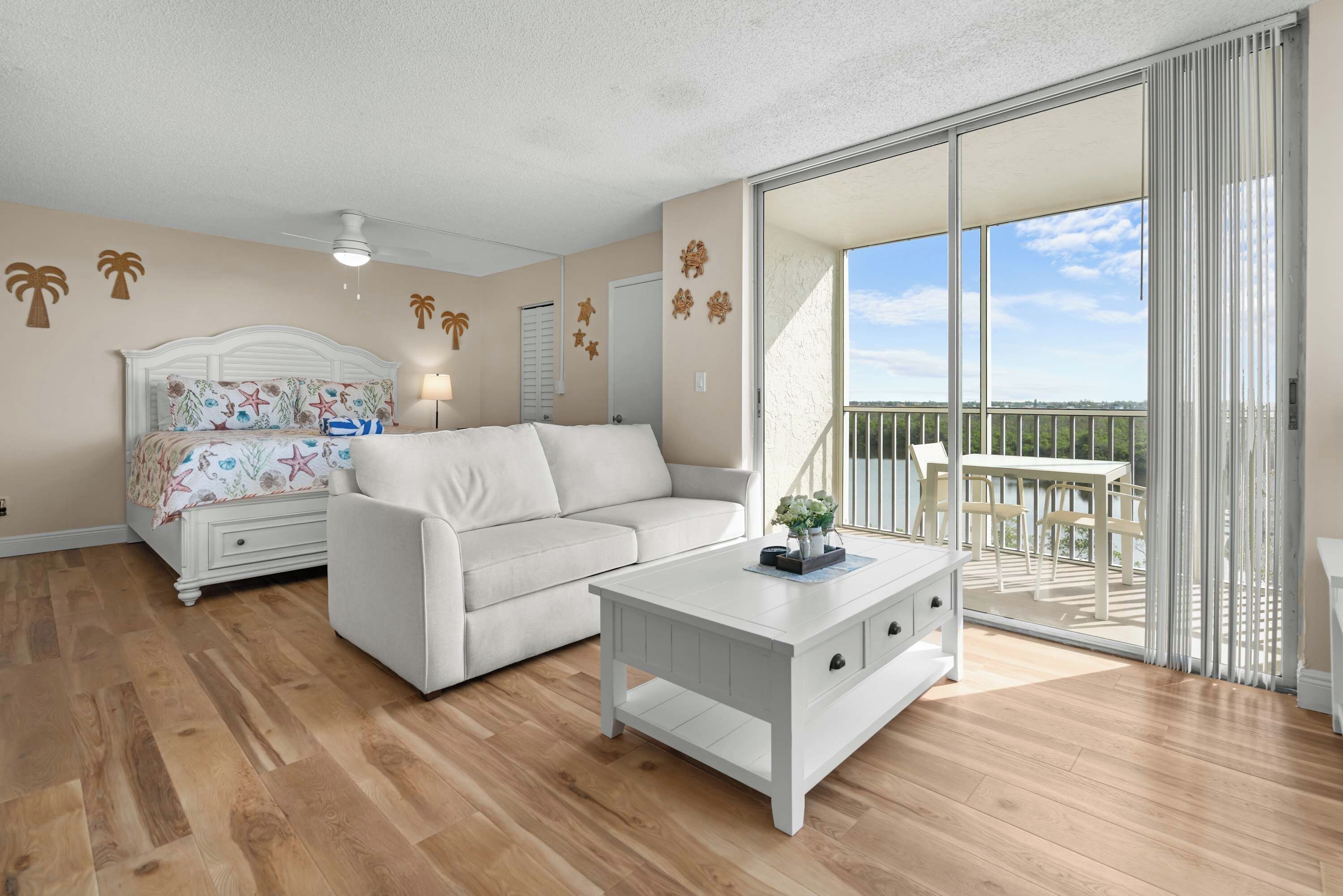 A room with a bed, a sofa, a small table, and a balcony with a view.
