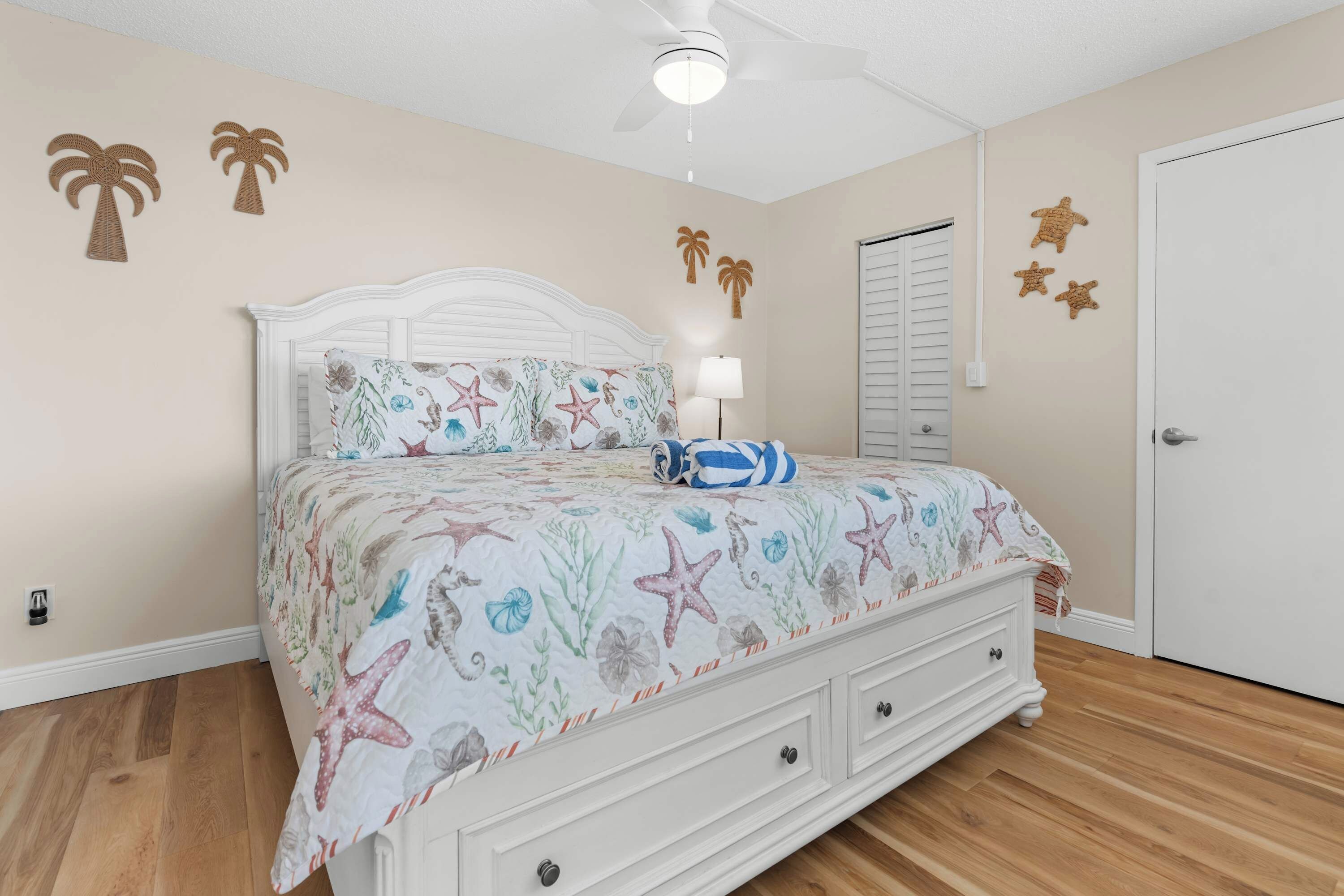 A bedroom with a bed, a nightstand, a ceiling fan, and a door.