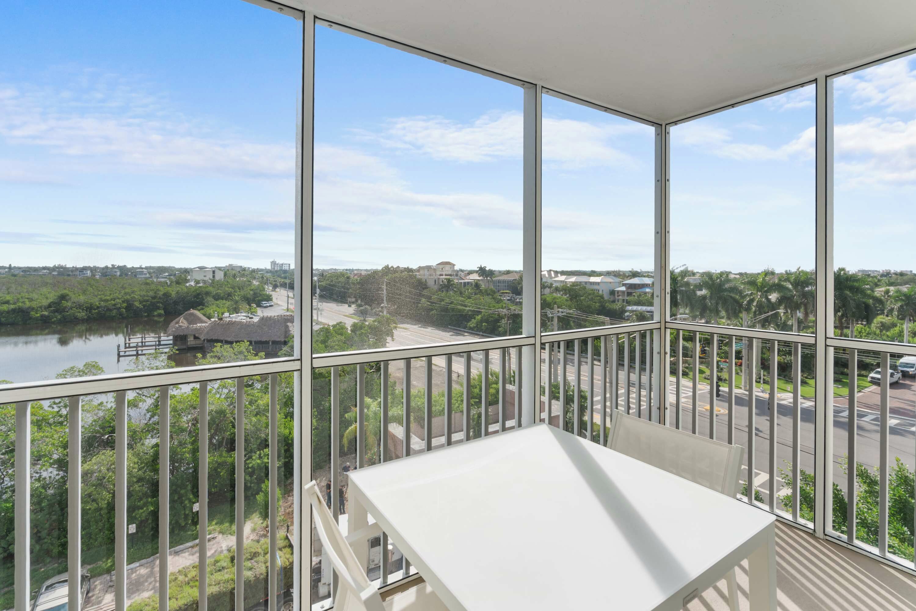 A balcony with a white table and a view of a river, buildings, and greenery.