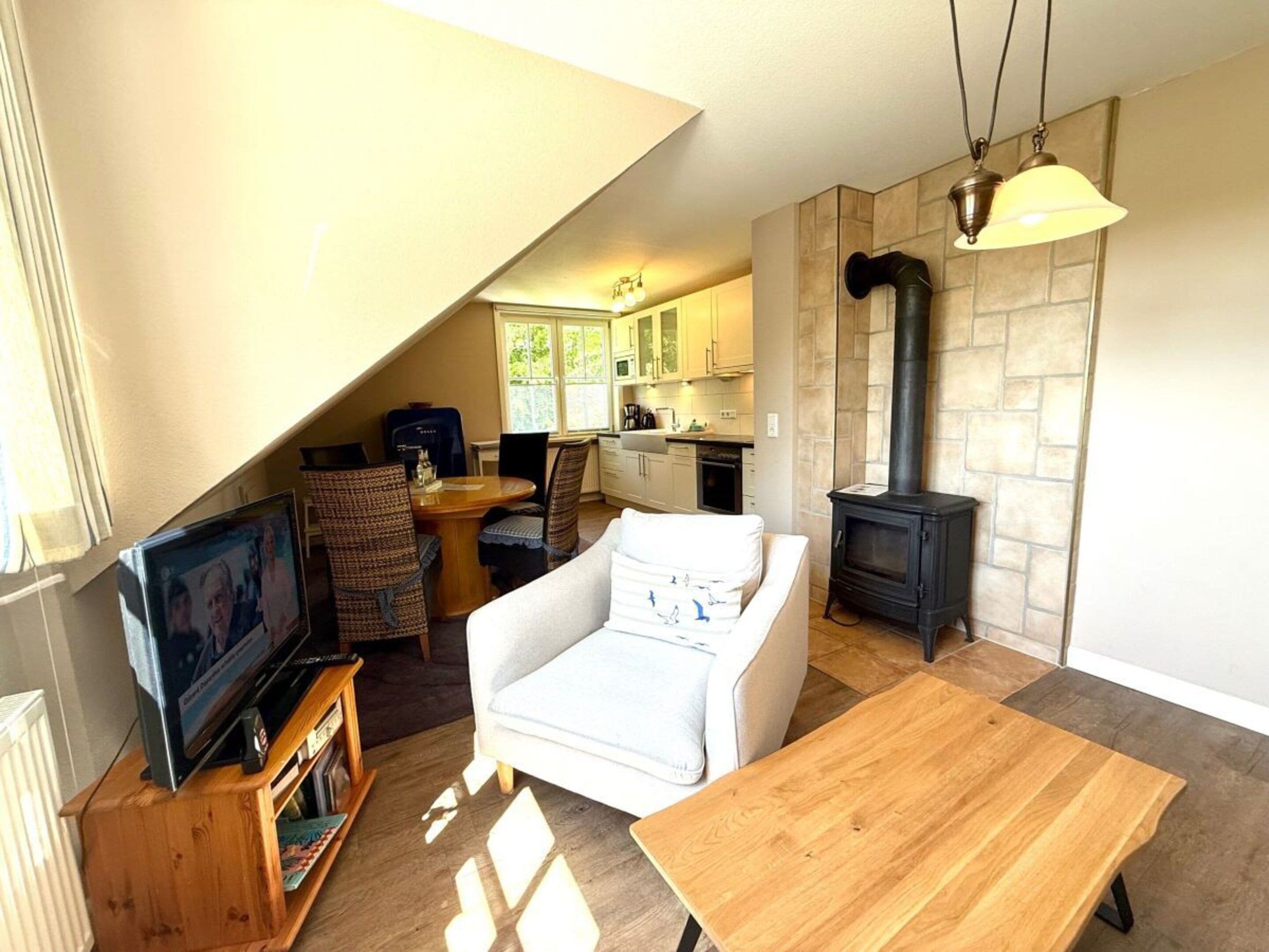 A cozy living room with a television, a sofa, a wooden table, and a kitchen in the background.