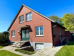 A red brick house with a green door, white windows, and a small porch. - Haus Heike - Holiday Apartment 1st Floor (Utersum)