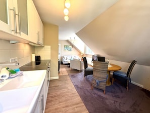 A modern kitchen with a dining area, a sofa, and a table with chairs. - Haus Heike - Holiday Apartment 1st Floor (Utersum)