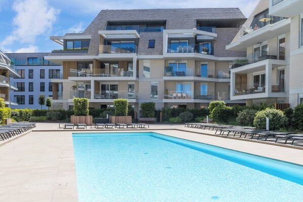 Een modern appartementencomplex met een zwembad, terras en balkons.