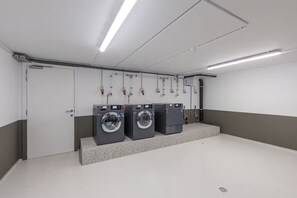 Une buanderie équipée de trois machines à laver, d’une porte et d’un éclairage au plafond.