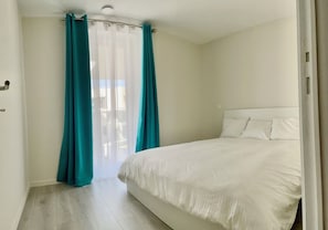 A bedroom with a bed, curtains, and a view through a window. - Villa Nordwind 0205 met garage (Nieuwpoort)