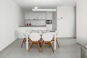 Een moderne keuken met witte kastjes, een eettafel met stoelen en een inbouwoven.