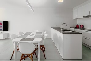 A modern kitchen with white cabinetry, a central island with a sink, and a dining area with a white table and chairs. - Villa Nordwind 0205 met garage (Nieuwpoort)