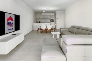 A modern living room with a flat-screen TV, a sofa, a dining area with a table and chairs, and a kitchen in the background. - Villa Nordwind 0205 met garage (Nieuwpoort)