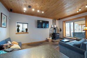 A living room with a stone fireplace, a large window, and a flat-screen TV mounted on the wall. - Mountain Retreat 5BR • Hot Tub • 25 Min to PC (Coalville)