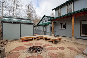 Ein Garten mit einer Holzbank, einem Feuerkorb und einem Haus mit Veranda.