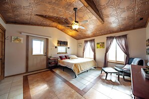 A bedroom with a bed, a desk, a chair, a ceiling fan, and a window.