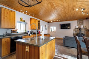 A spacious kitchen with wooden cabinets, a central island, and a stone fireplace. - Mountain Retreat 5BR • Hot Tub • 25 Min to PC (Coalville)