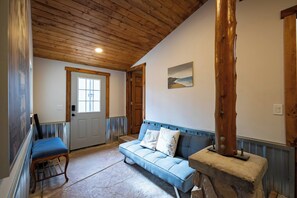 Ein Zimmer mit Holzbalkendecke, einem blauen Sofa mit Kissen, einem Holzstuhl und einer Tür mit Fenster.
