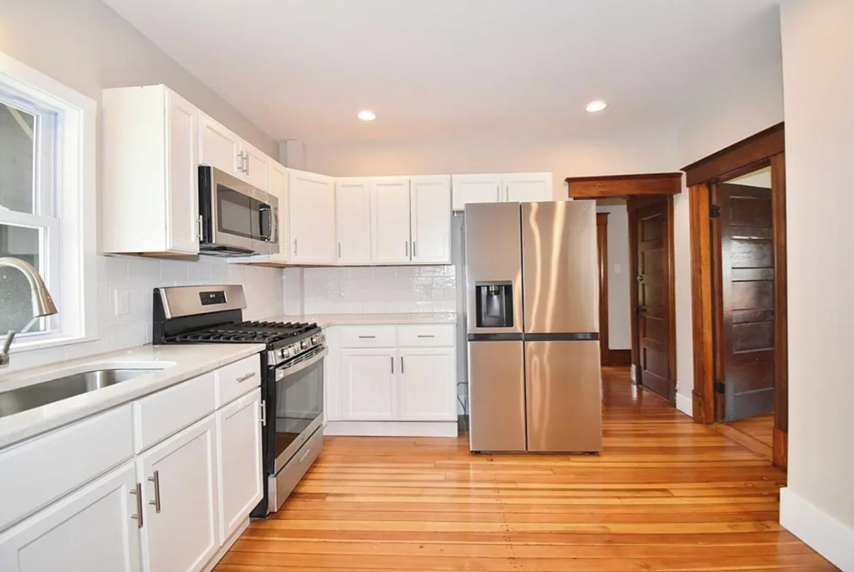 A modern kitchen with white cabinetry, stainless steel appliances, and a wooden floor.