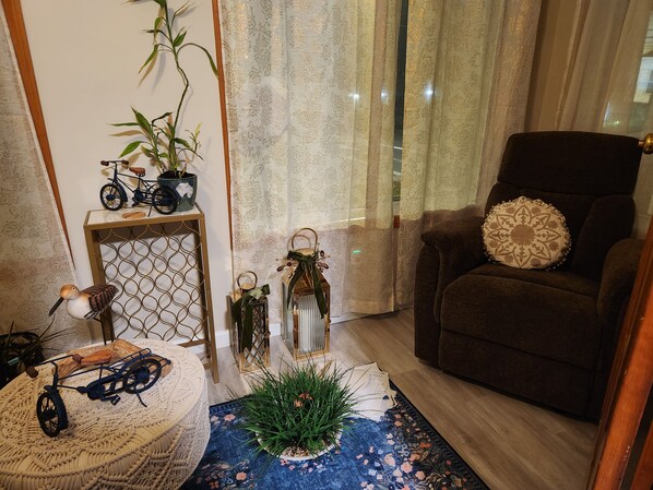 Een gezellige woonkamer met een bruine fauteuil, een bijzettafeltje met decoratieve objecten, een fiets en een potplant.