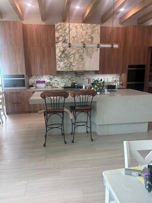 A modern kitchen with wooden cabinets, a marble backsplash, and a central island with bar stools. -  Room with ultra-modern amenities . Newly built house -facing Tampa river. (Tampa)