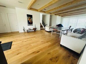 Uma sala de estar ampla com piso de madeira, um sofá branco, uma mesa de jantar e uma escada que leva a outro nível.