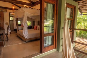 A bedroom with a canopy bed, a wooden floor, and a view of greenery outside. - 4-bedroom house in fabulous Trancoso with AC and fitness room (Trancoso)