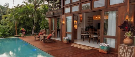 A wooden deck with a pool, outdoor furniture, and a dining area with chairs and tables.