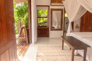 A room with a bed, a wooden bench, a small table, and a view of greenery outside. - 4-bedroom house in fabulous Trancoso with AC and fitness room (Trancoso)