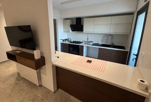 A modern kitchen with white cabinets, a countertop, and a TV mounted on a wooden shelf. - Elegant Apartment (Tunis)