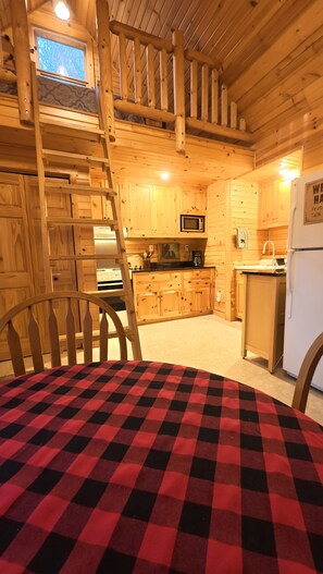 Interior de fusta amb taula de dinar, cuina amb armaris de fusta, microones i nevera.