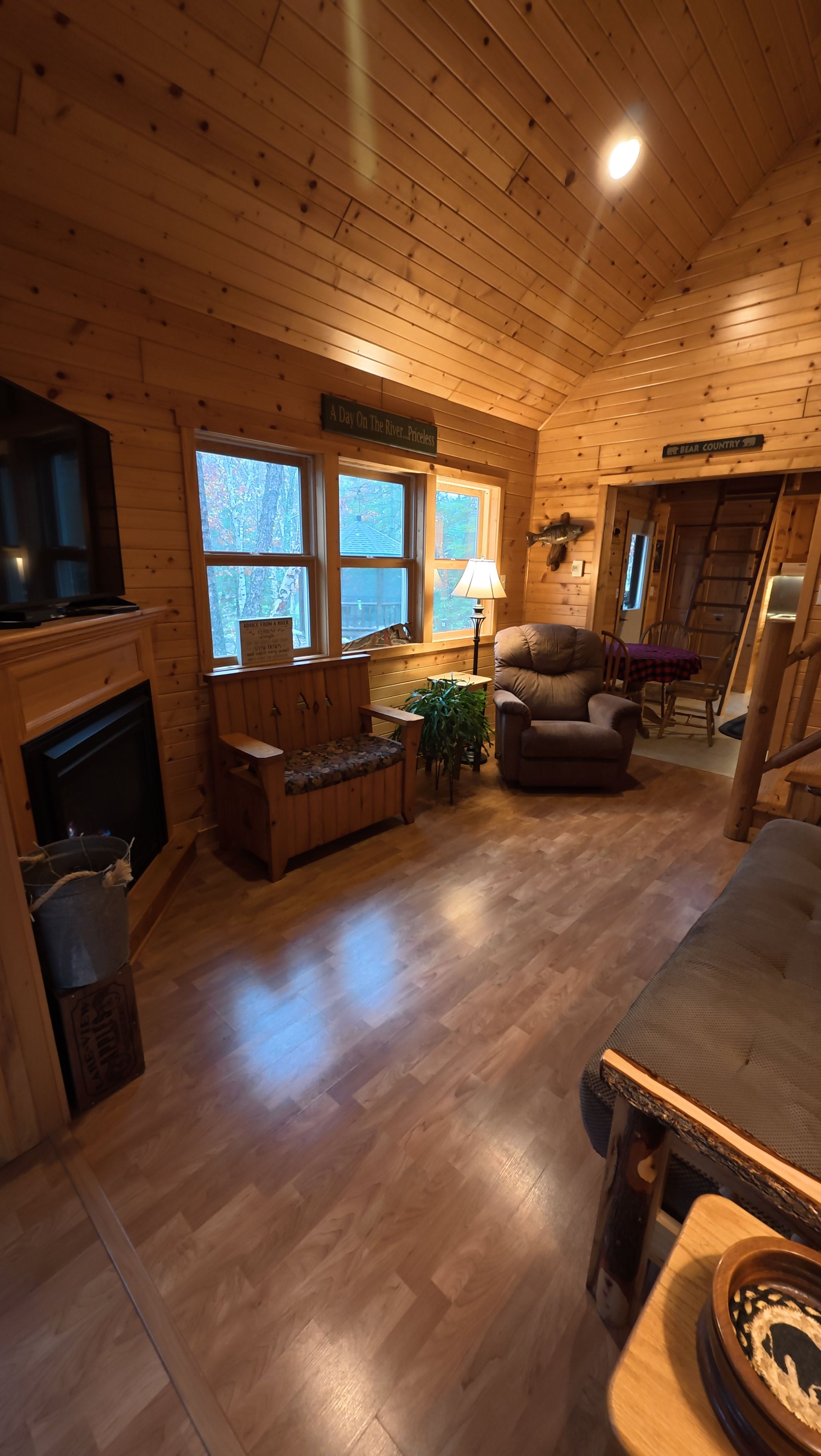 Interior de una cabaña de madera con chimenea, zona de estar y televisor.
