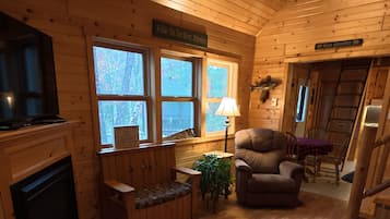 Interior de una cabaña de madera con chimenea, zona de estar y televisor.