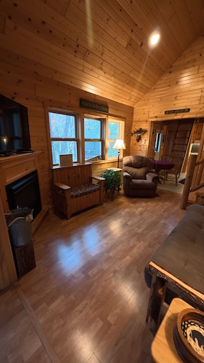 L'intérieur d'un chalet en bois comprend une cheminée, un coin salon et un téléviseur.