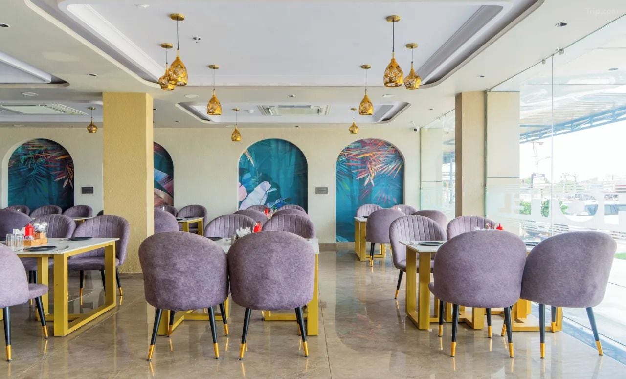 Un restaurante con sillas moradas y detalles dorados, que cuenta con grandes ventanales y obras de arte en las paredes.