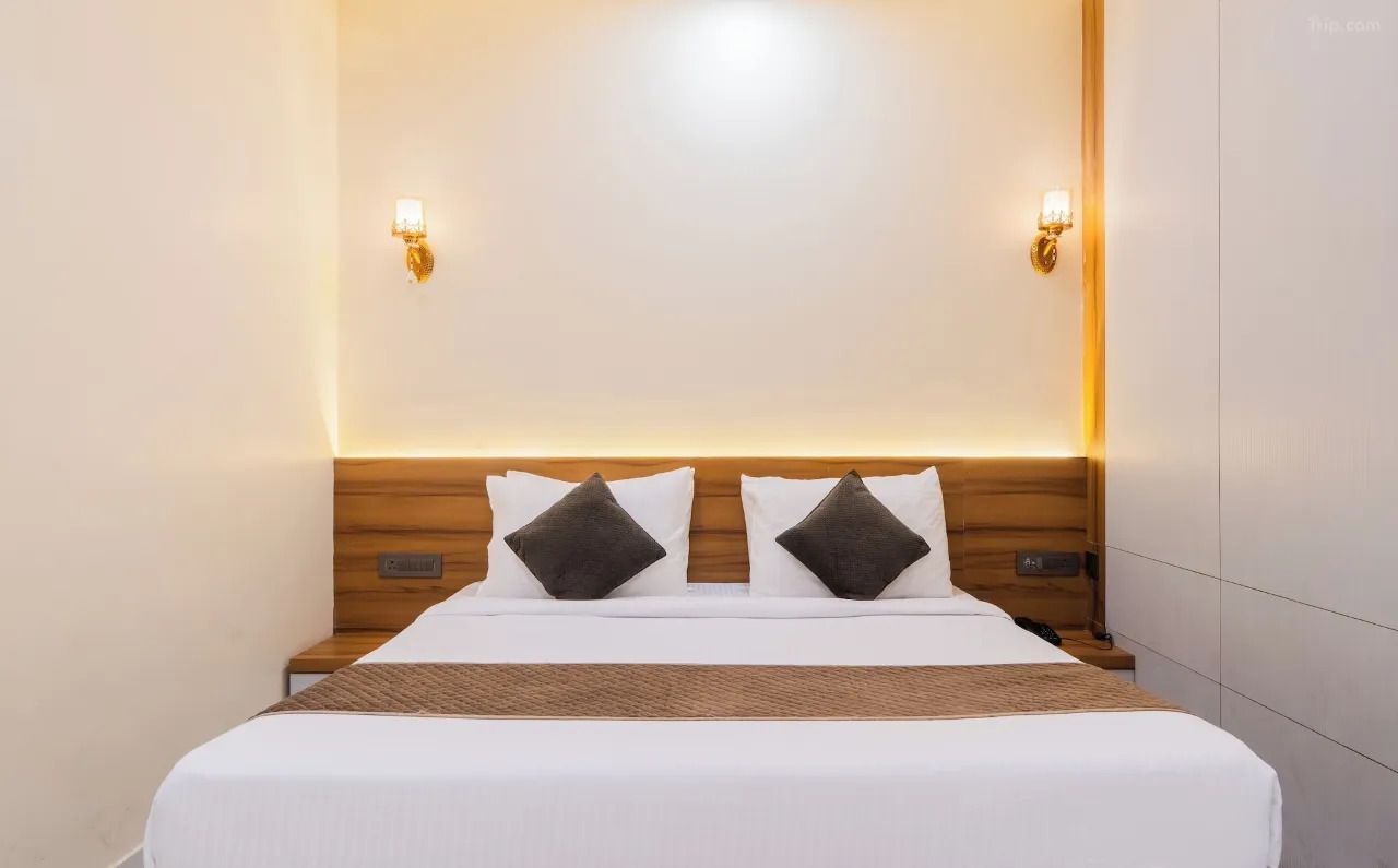 Una habitación de hotel con cama, dos lámparas fijadas a la pared y un cabecero de madera.