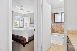 Une chambre à coucher avec un lit, un ventilateur de plafond, une fenêtre avec des rideaux et une vue sur l’extérieur.