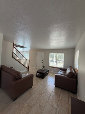 A spacious living room with two sofas, a coffee table, and a staircase leading to an upper level.