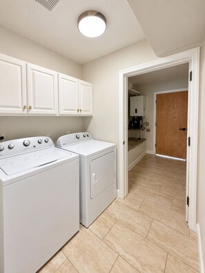 A laundry room with two front-loading washers and dryers, white cabinets above, and a wooden door leading to another room.