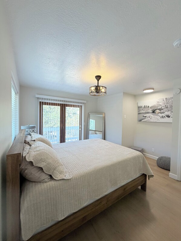 A bedroom with a large bed, a ceiling light fixture, a window with blinds, and a wall-mounted picture.