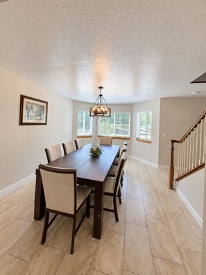 A dining room with a large table, chairs, a chandelier, and windows.