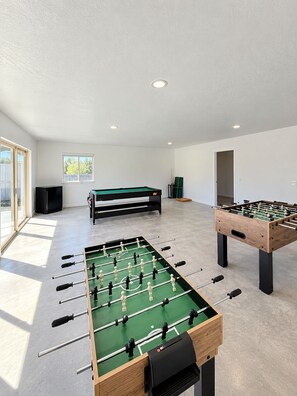 A room with two foosball tables, a pool table, and a billiards table.