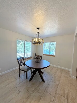 A dining area with a round table, chairs, a chandelier, and large windows.
