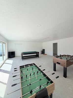 A spacious room with two foosball tables, a billiards table, and a television.