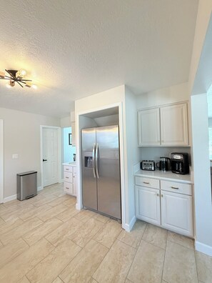 A modern kitchen with a stainless steel refrigerator, white cabinetry, and a built-in coffee maker.