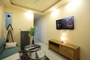 A living room with a television mounted on the wall, a small table, a sofa, a cabinet, and a plant. - Forest view 1BHK Premium studio appartment (New Delhi)