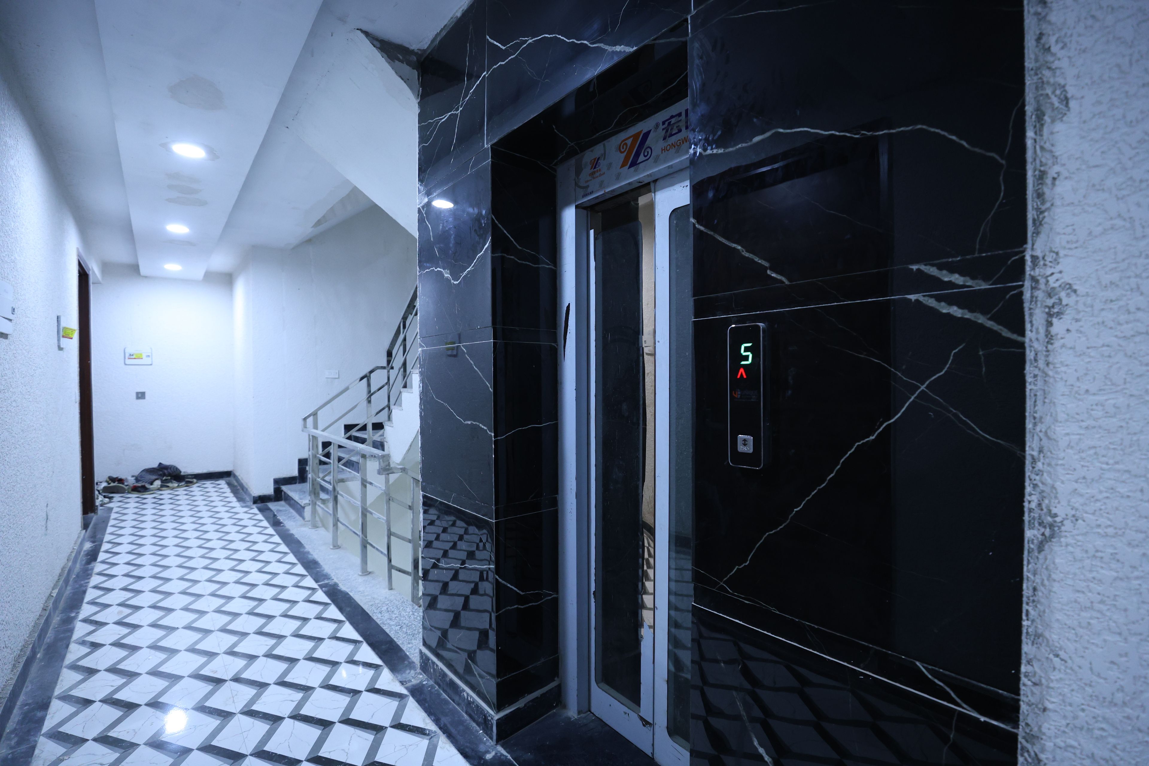 Een gang met betegelde vloer, een trap en een lift met een digitaal scherm.